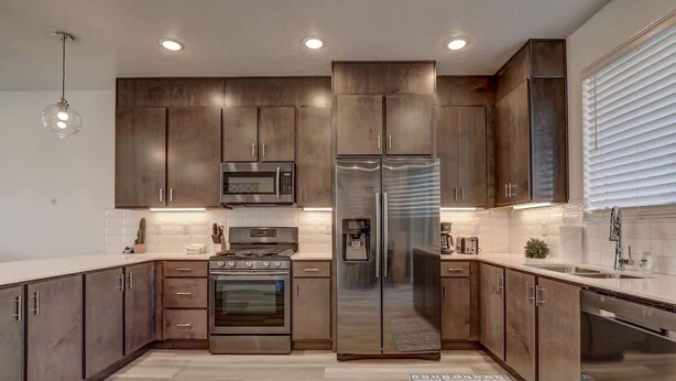 A modern kitchen with dark wood cabinets, stainless steel appliances, and a patterned rug. - The Lofts #36 | Townhome Pool Resort (Saint George)