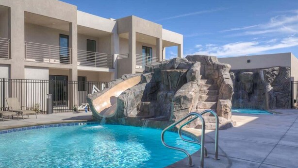 A pool with a water slide, a rock formation, and a modern building with balconies. - The Lofts #36 | Townhome Pool Resort (Saint George)