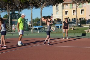 Un terrain de tennis extérieur avec un filet, des bancs et un bâtiment en arrière-plan.