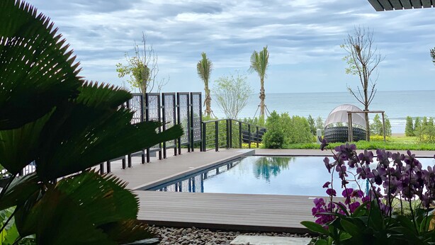 A pool area with a view of the sea, surrounded by tropical plants and a pergola structure. - Gorgeous Sunset View ❤︎ Mae Phim Beachfront Condo (Kram)