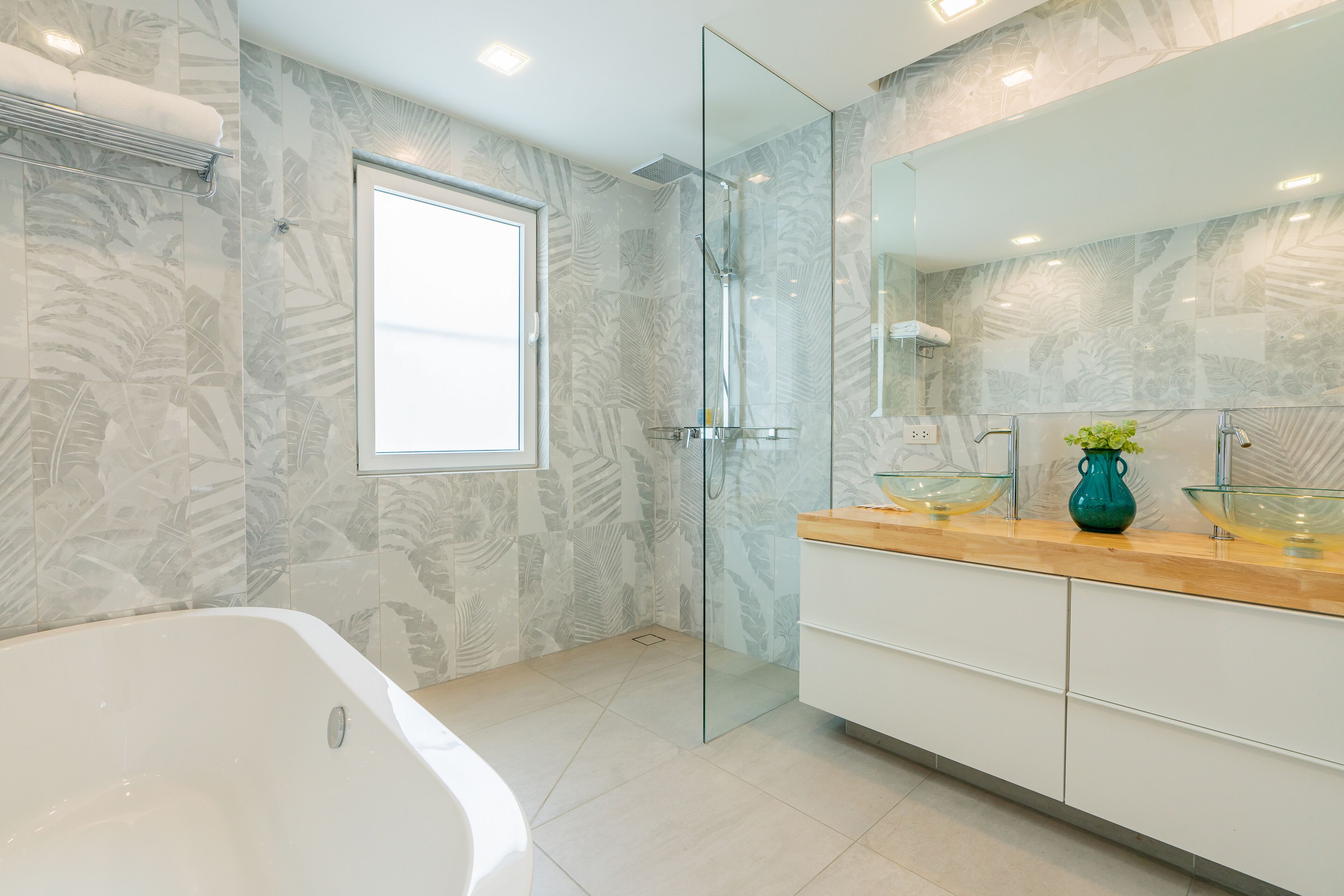A modern bathroom with a glass shower enclosure, a large bathtub, and a vanity with a mirror and glass bowl sink.