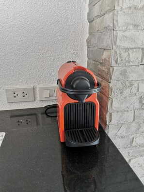 A red appliance with a black front panel, possibly a toaster, on a black countertop next to a white textured wall and a stone wall.