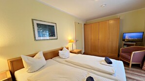 Hotellihuone, jossa on kaksi sänkyä, televisio, puinen vaatekaappi ja tuoli.