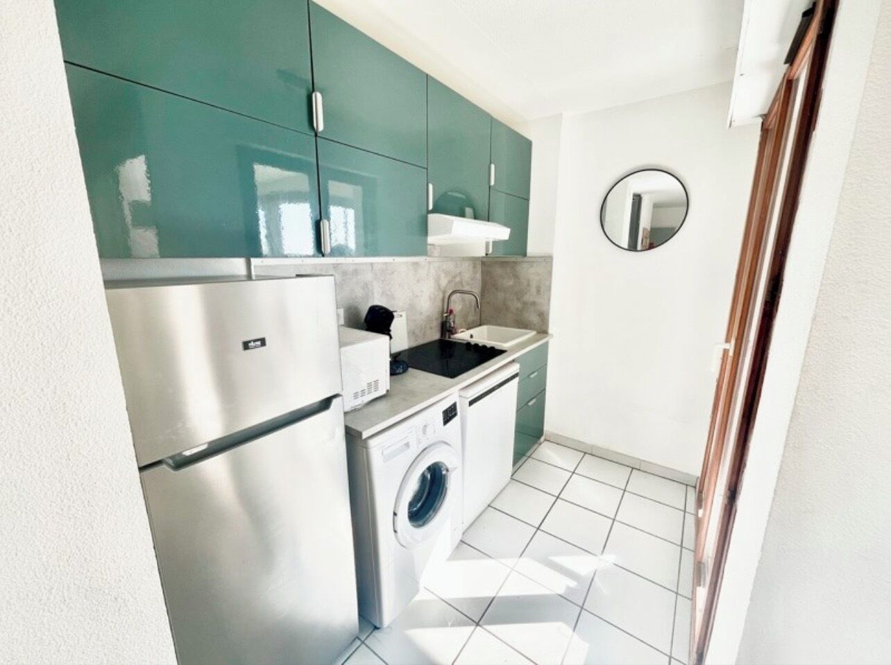 Une cuisine compacte dotée d’un réfrigérateur en acier inoxydable, d’un lave-linge, d’un évier et de meubles de couleur turquoise.