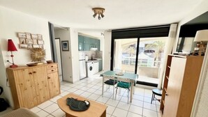 Ett kompakt bostadsutrymme med ett litet kök, en matplats och utsikt genom ett stort fönster.