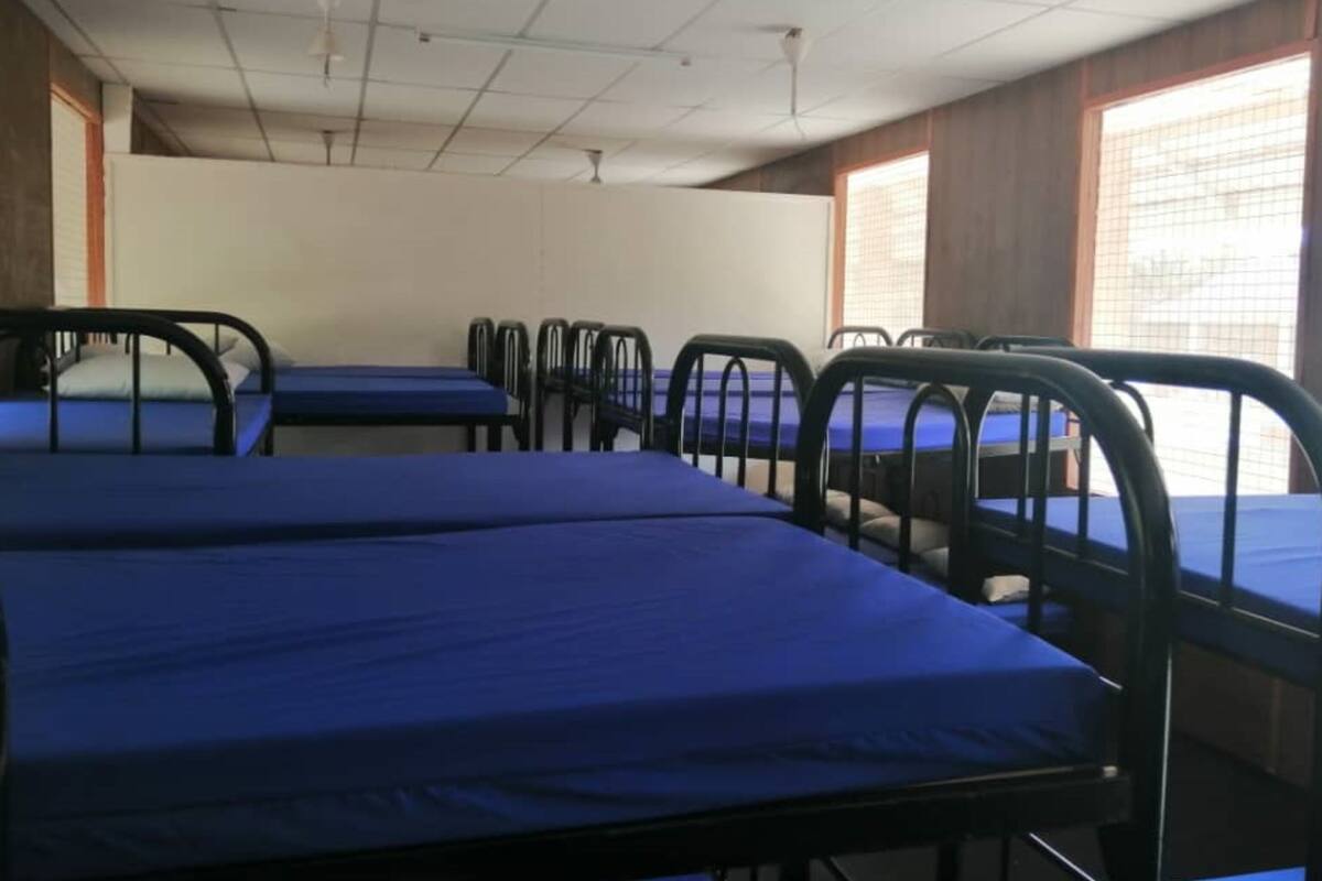 Ein Schlafsaalzimmer mit Etagenbetten und Schreibtischen, einer gefliesten Decke und Fenstern mit Jalousien.