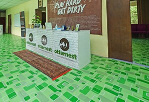 A reception desk with a white counter, a green patterned floor, and a wall with a large poster advertising outdoor activities. - Hotel O Otternest @ Gunung Pulai 2 (Pekan Nanas)