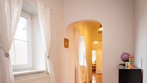 A hallway with wooden flooring, white walls, and a window with white curtains. - Ferienwohnung ALEX (Burgau)