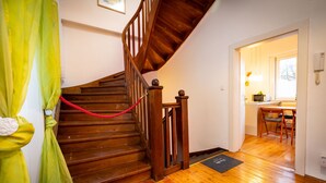 A wooden staircase with a red rope barrier, leading to a room with a wooden floor and a dining area visible through an open door. - Ferienwohnung ALEX (Burgau)