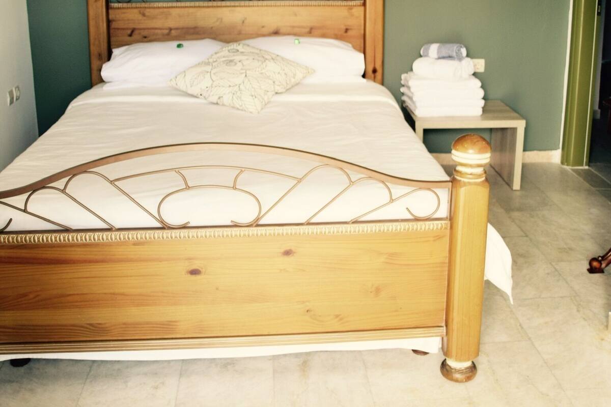A neatly made bed with a wooden headboard and a decorative metal frame, a bedside table with folded towels, and a hanging light fixture.