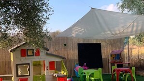 Une cabane de jeu avec un toboggan, une petite table et une tente, installée dans un jardin.