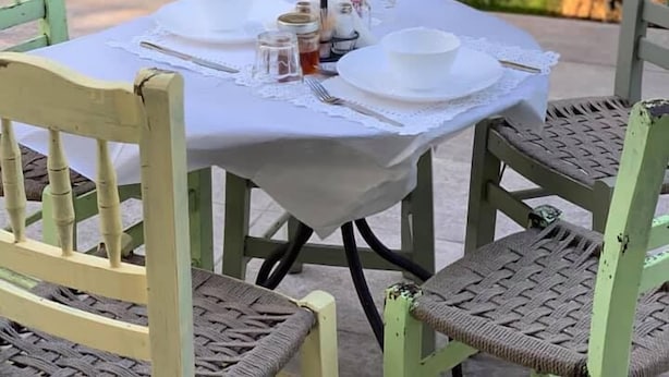Une table à manger d’extérieur, dressée pour quatre personnes, avec une nappe blanche, des assiettes et des couverts.