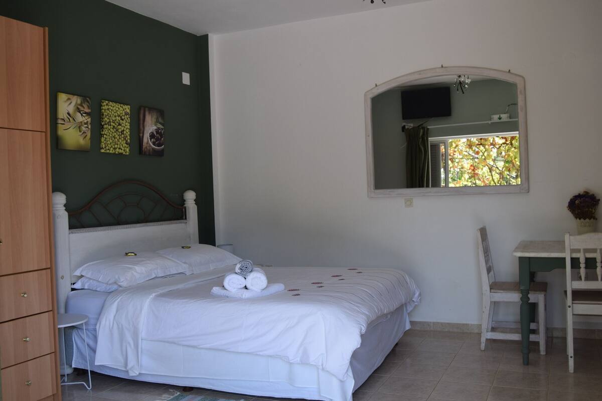 A bedroom with a bed, a chair, a table, and a mirror.