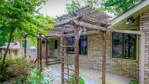 Ein überdachter Patio-Bereich mit einer Holz-Pergola, Ziegelmauern und Topfpflanzen.