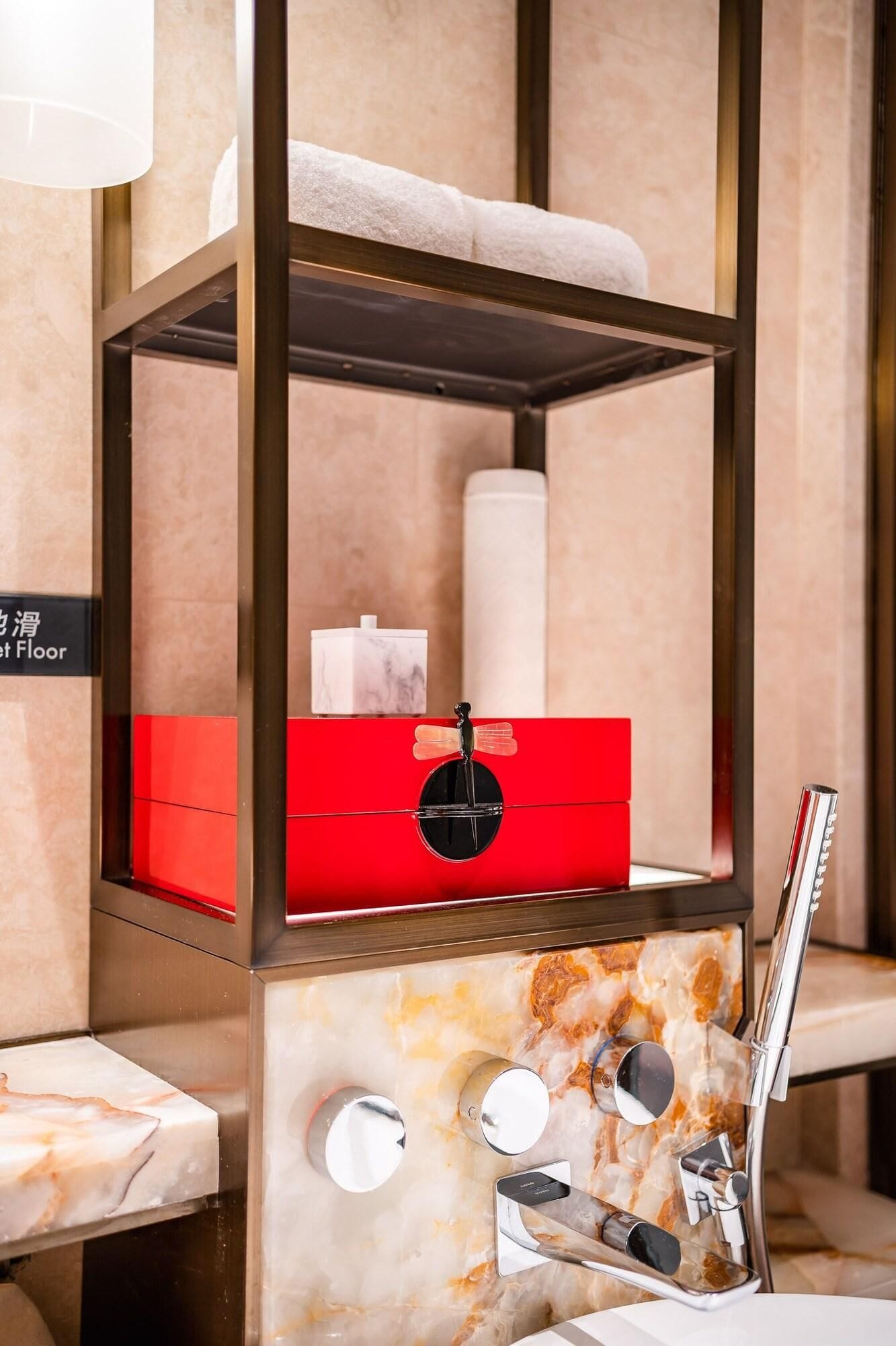 Un lavamanos de baño con encimera de mármol, una caja roja de almacenamiento, un adorno negro y un grifo moderno.