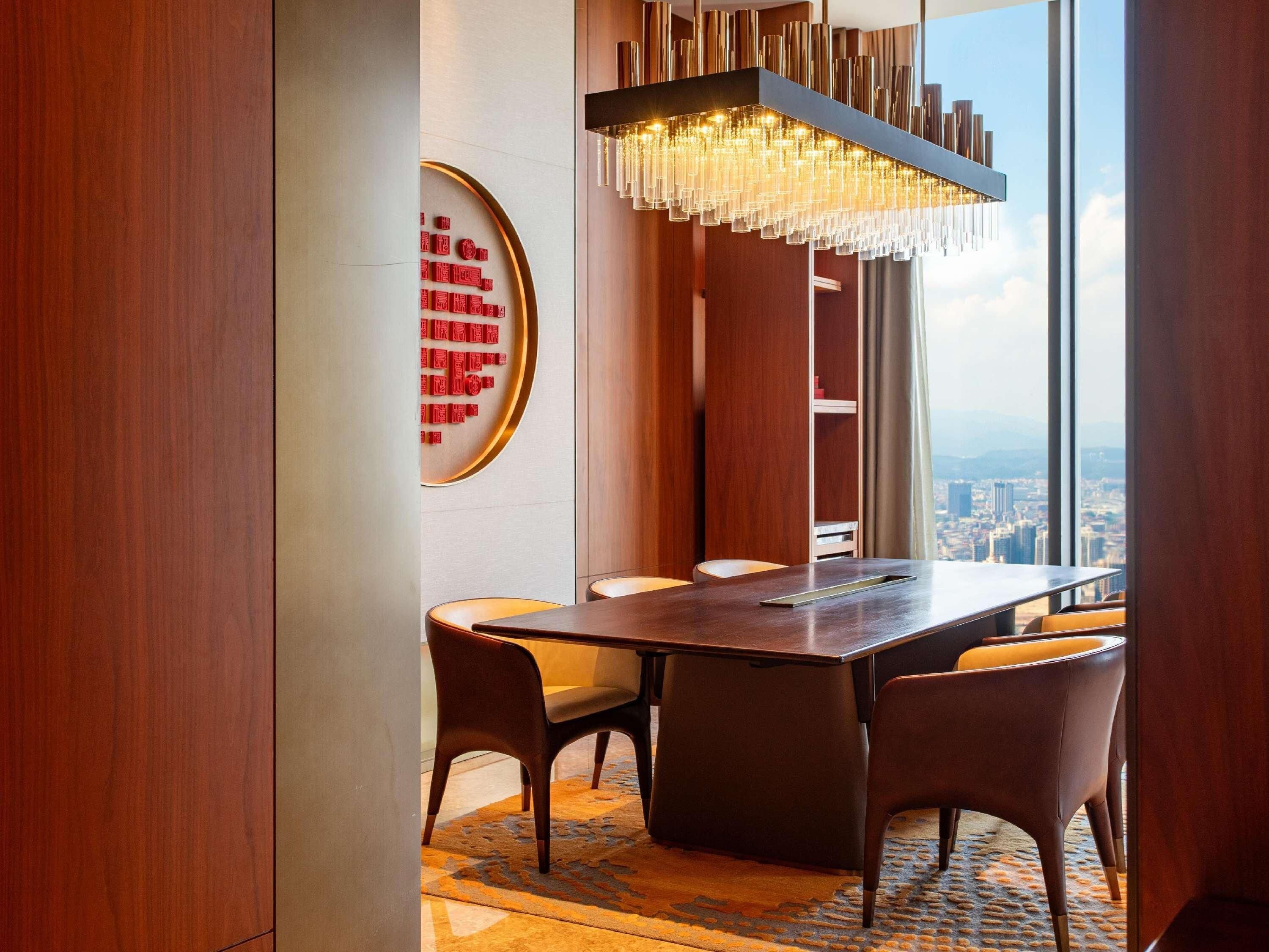 A modern dining area with a long table, chairs, and a city view through large windows.