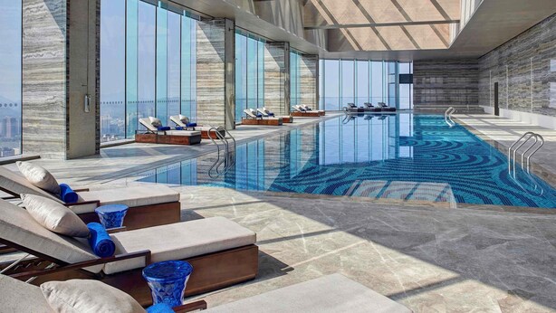 A modern indoor pool area with sun loungers, a clear pool, and large windows. - Pullman Huizhou Kaisa (Huizhou)
