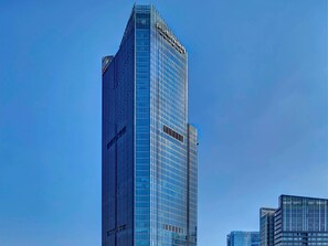 A tall, modern skyscraper with a reflective glass facade, surrounded by other buildings. - Pullman Huizhou Kaisa (Huizhou)