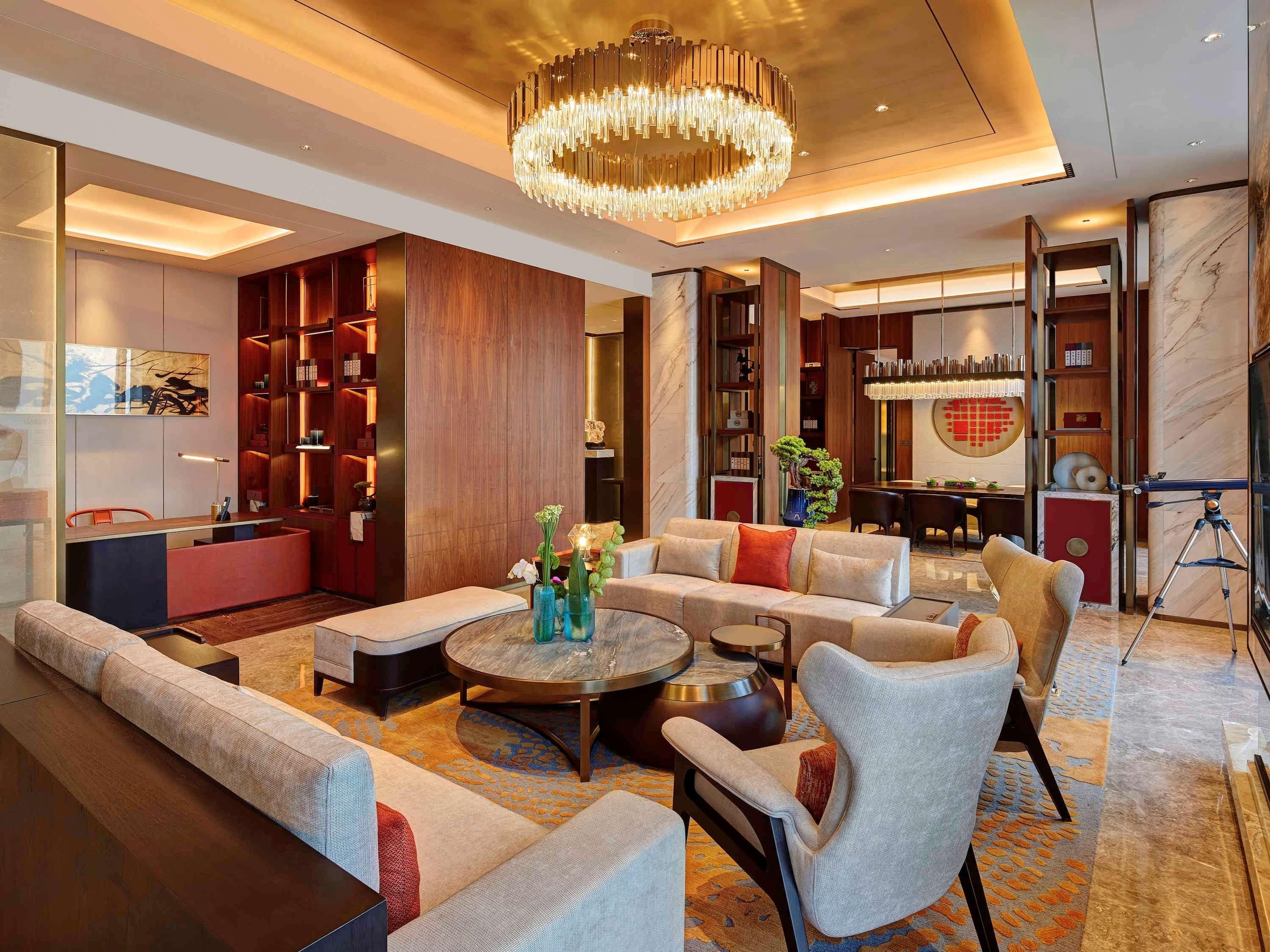 Eine moderne Hotellobby mit einer zentralen Sitzecke, einem großen Kronleuchter und einem marmornen Empfangstisch.