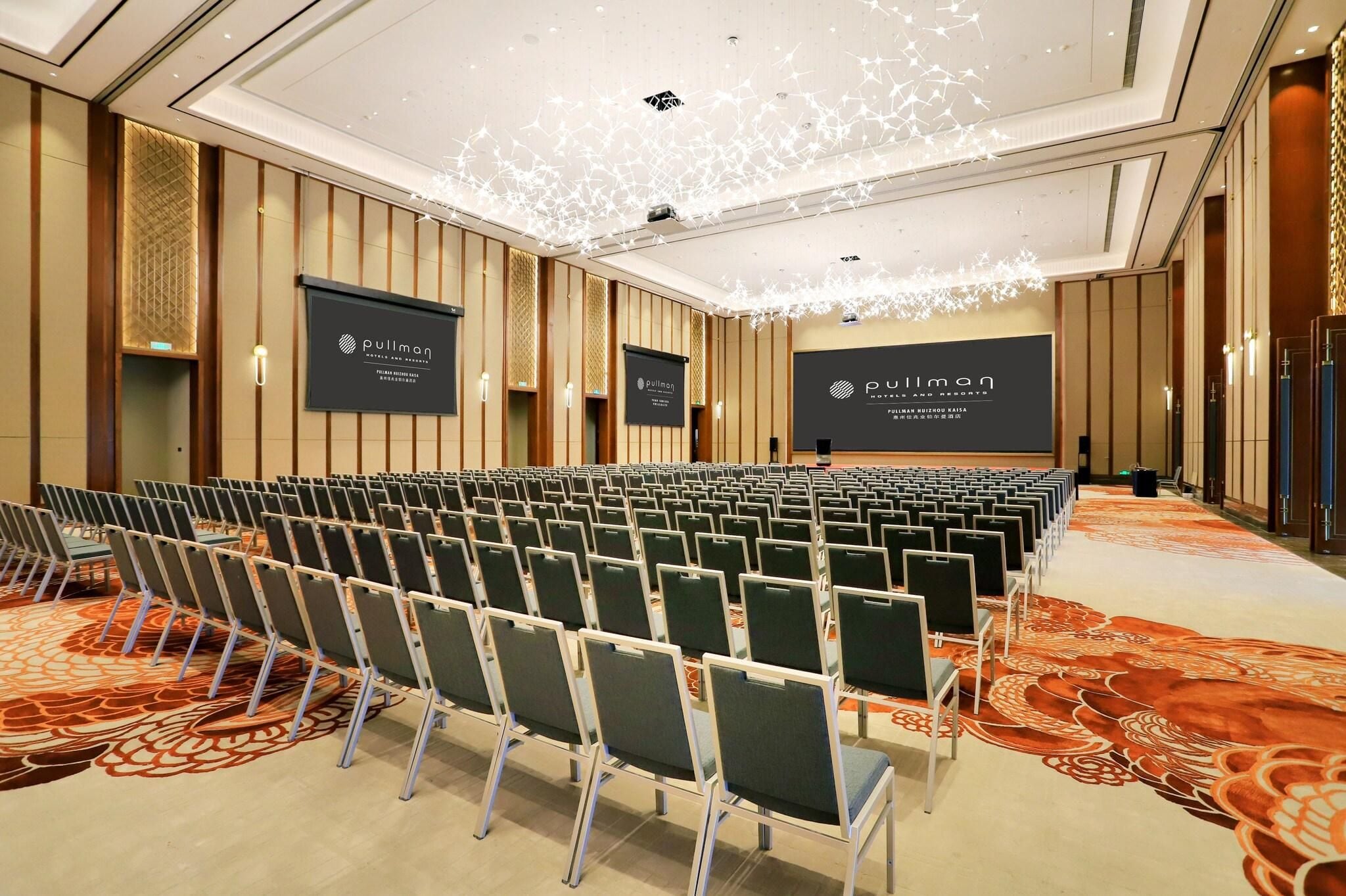 A conference room with rows of chairs, a large screen, and a patterned carpet.