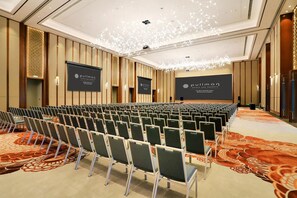A conference room with rows of chairs, a large screen, and a patterned carpet.