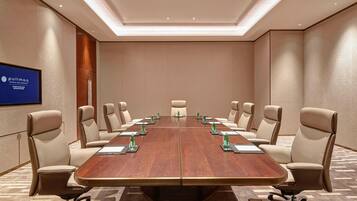Un salón de conferencias con una larga mesa, sillas color beige y un cartel de tipo pullman en la pared.