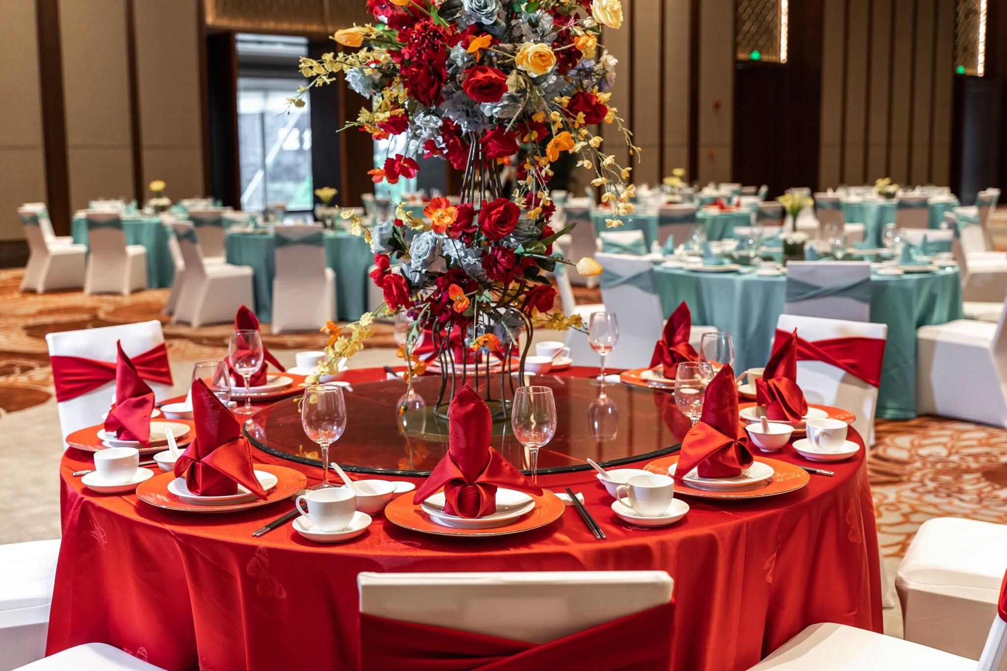 Un salón de banquetes con mesas redondas, manteles rojos y sillas blancas.