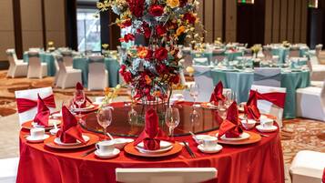 Un salón de banquetes con mesas redondas, manteles rojos y sillas blancas.