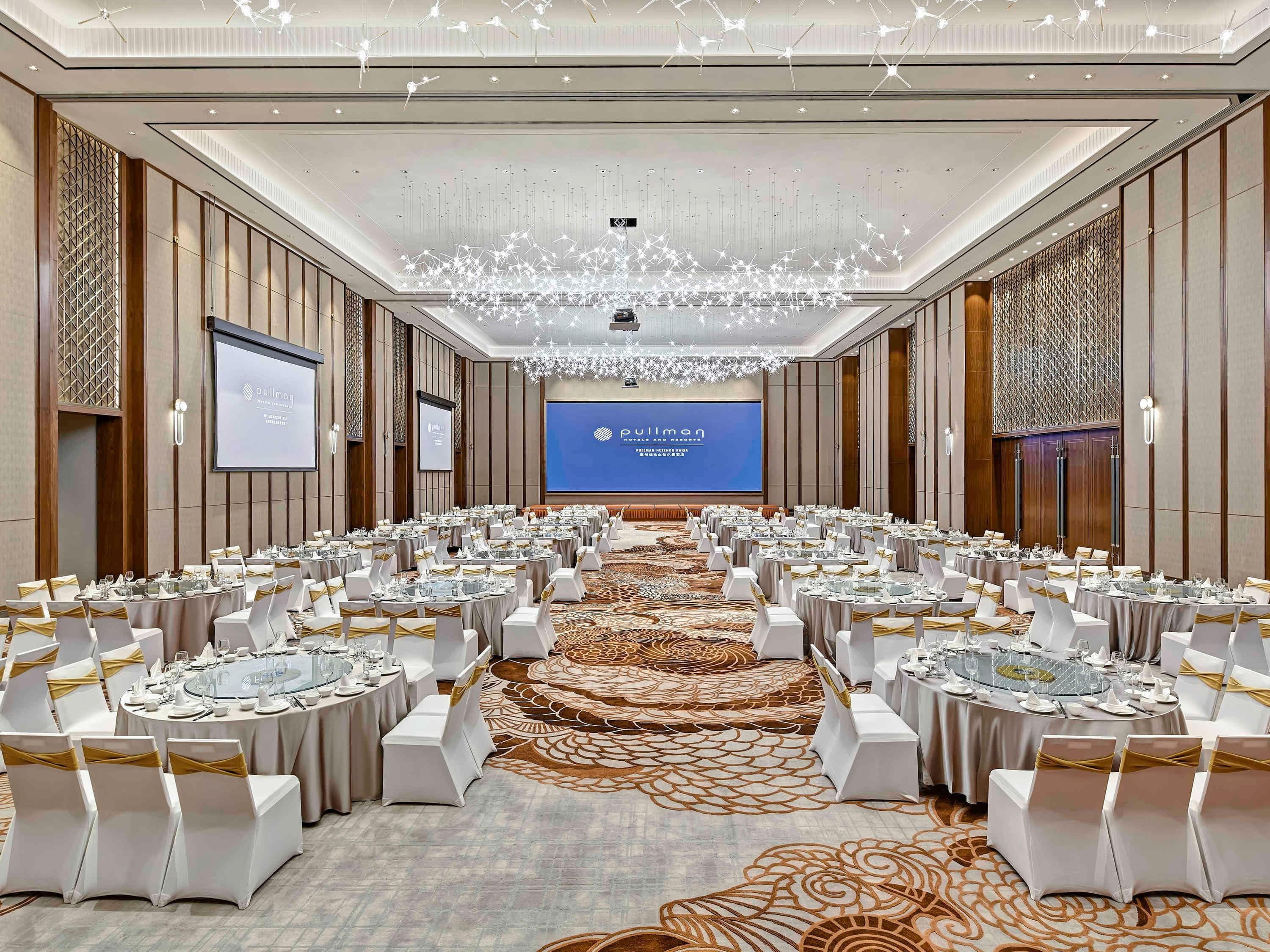 Un salón de conferencias con mesas redondas, sillas blancas y una pantalla grande que muestra 'Pullman'.
