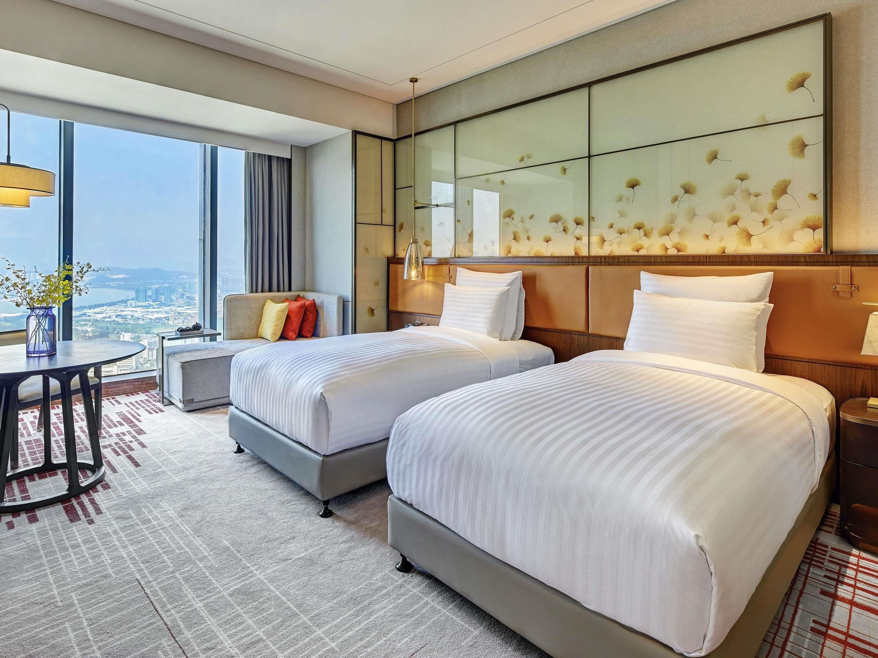 Une chambre d’hôtel avec deux lits, une vue sur la ville, un coin repas et une grande fenêtre.