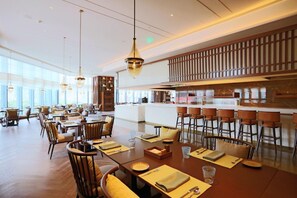 A spacious dining area with high tables, chairs, and hanging pendant lights.