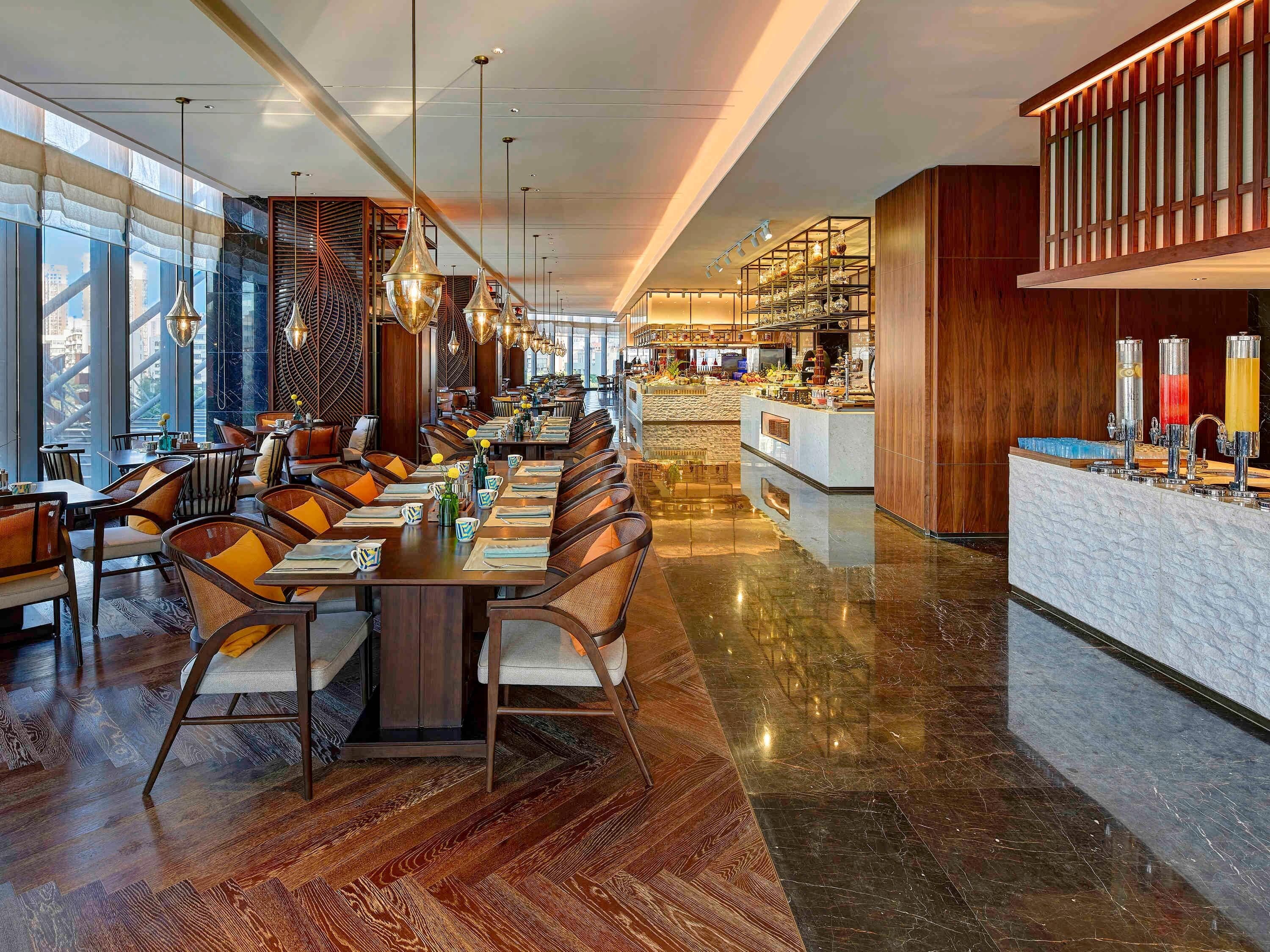 A spacious dining area with high ceilings, modern chandeliers, and a central island with a bar.