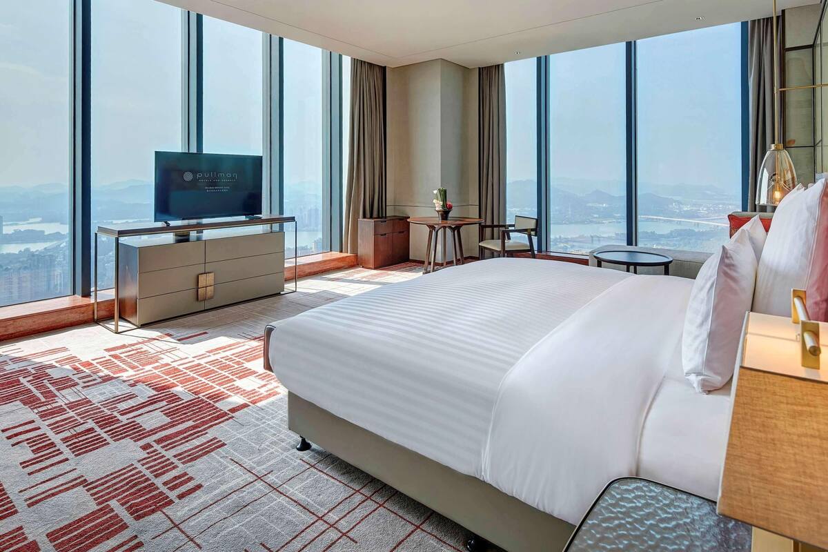 Quarto de hotel com cama grande, televisão, escrivaninha e vista para a cidade.