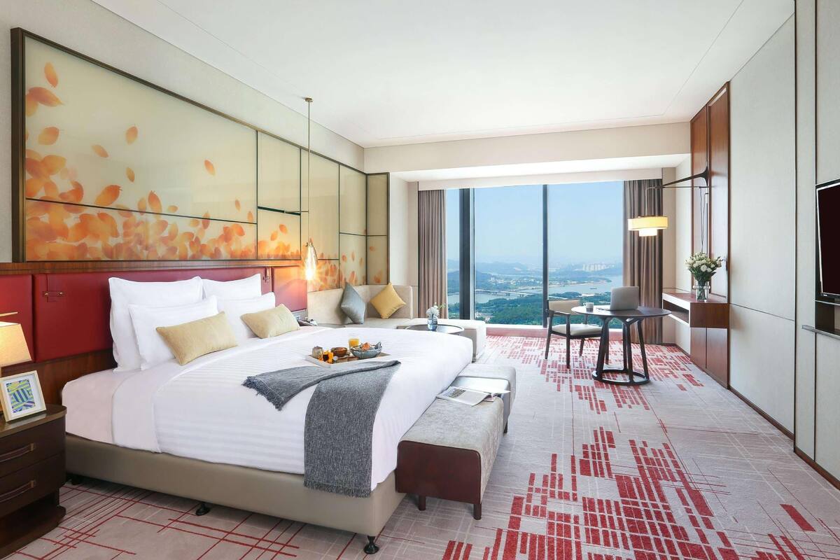 Quarto de hotel com uma cama grande, uma escrivaninha, uma cadeira, uma televisão e vista para a cidade.