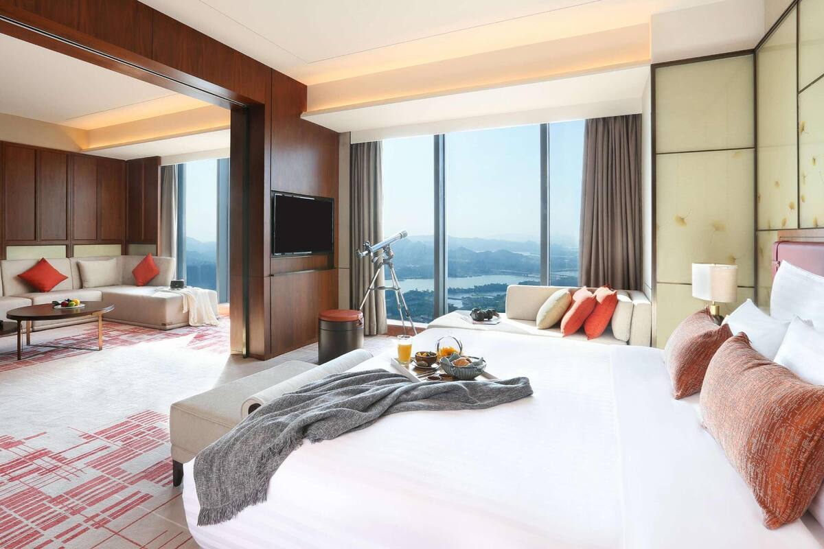 Quarto de hotel com uma cama grande, um sofá, uma televisão, um telescópio e vista para as montanhas.