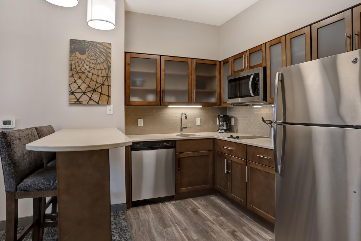 A modern kitchen with wooden cabinets, a stainless steel refrigerator, a dishwasher, and a microwave.