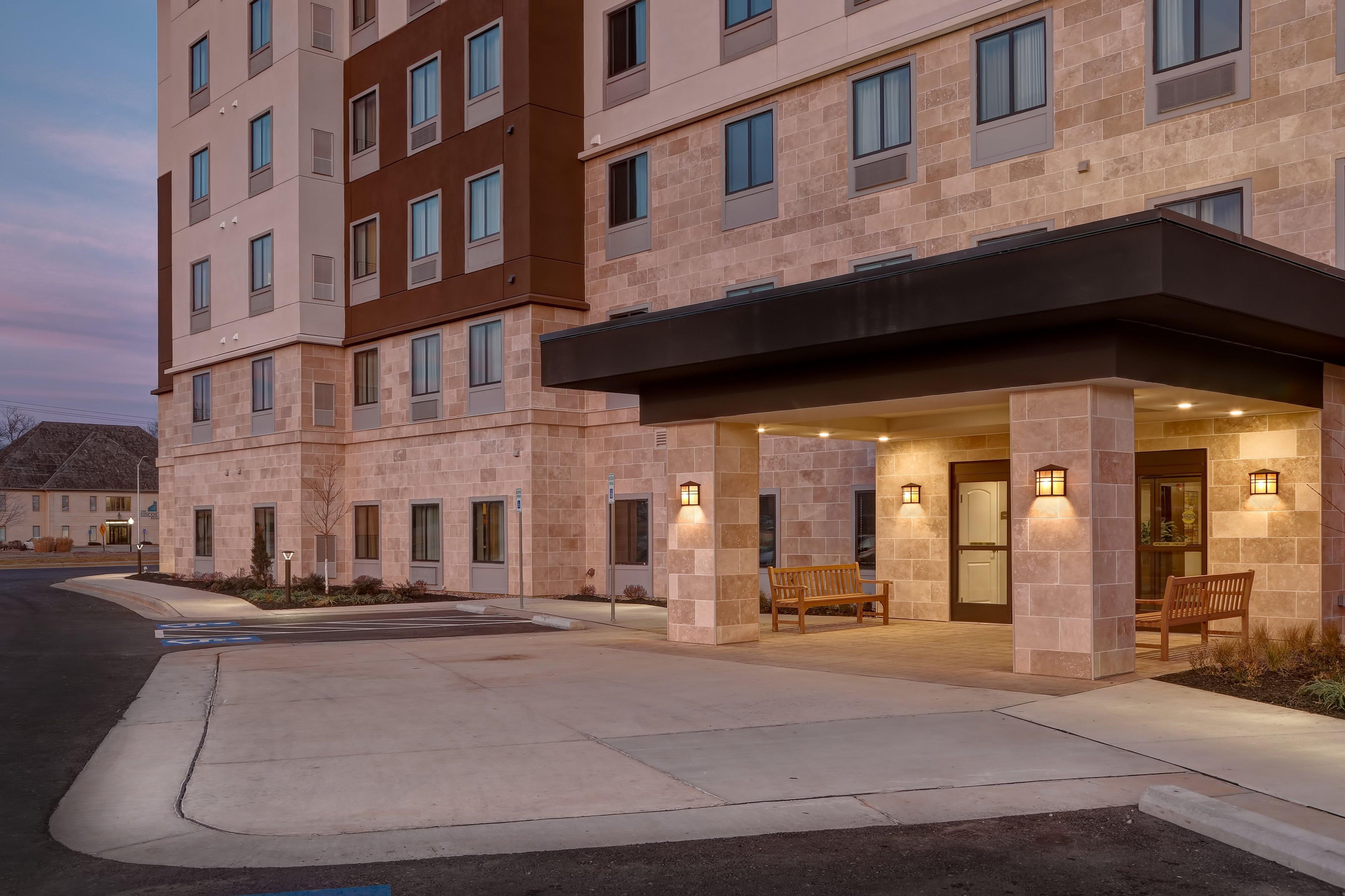 Un hotel de varios pisos con entrada cubierta, mobiliario exterior y zona de estacionamiento.
