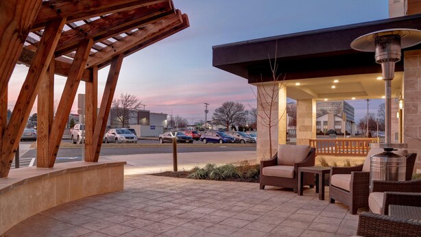 A covered outdoor seating area with wicker furniture, a gas station in the background, and a clear sky. - Staybridge Suites Overland Park - Kansas City S (Overland Park)