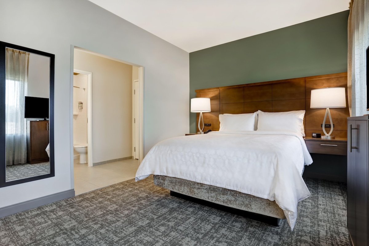 A hotel room with a bed, two bedside lamps, a nightstand, a mirror, and a door leading to a bathroom.