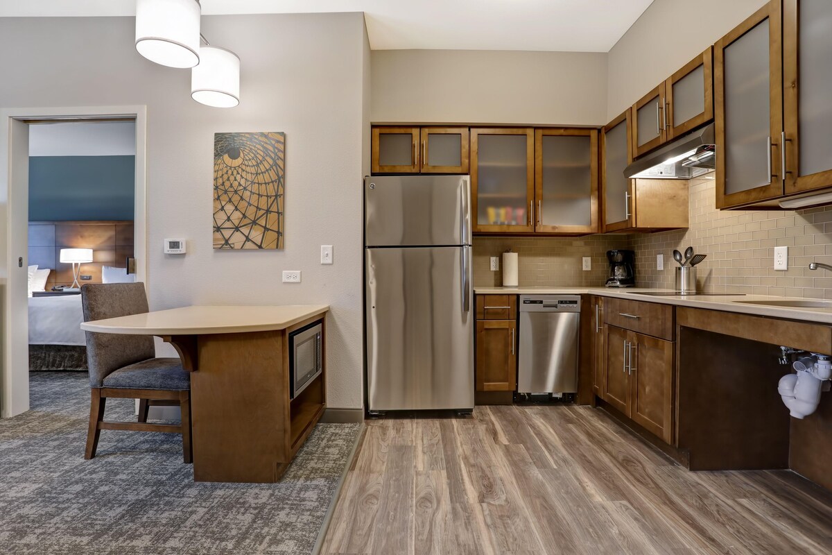 A modern kitchen with wooden cabinets, a stainless steel refrigerator, and a dining area with a table and chair.