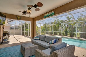 A sunlit indoor space with a pool, wicker furniture, and a ceiling fan.