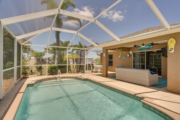 A covered outdoor swimming pool with a patio area, a lounge chair, and a surfboard decoration.