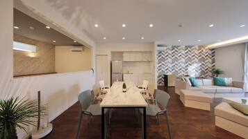 A modern living room with a dining area, a sofa set, and a kitchen in the background.
