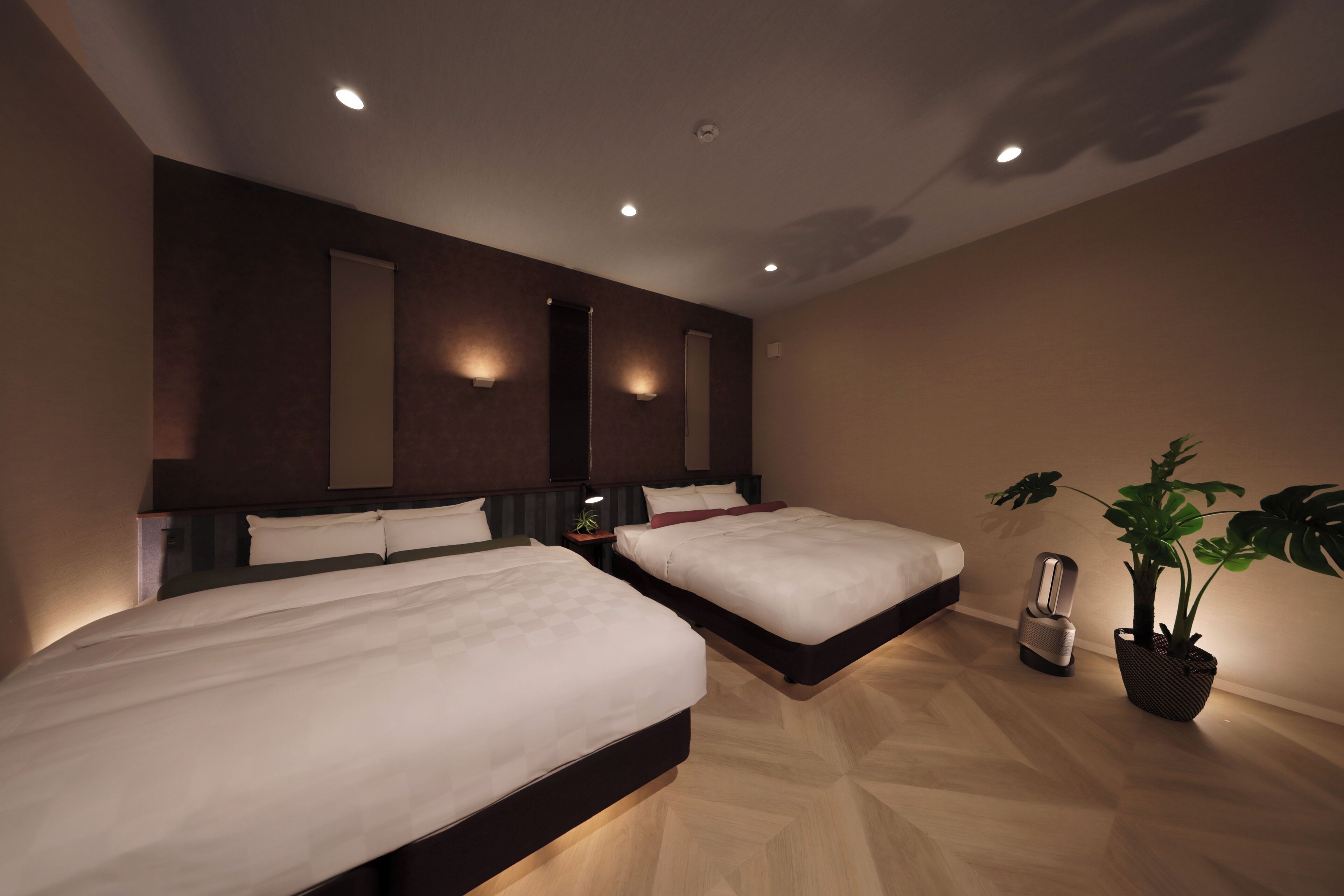 Una habitación de hotel moderna con dos camas, una planta en maceta y una mesita de noche con lámpara.