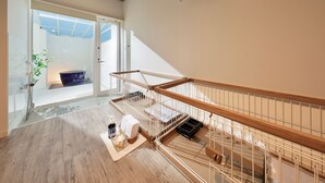 Ein geräumiger Innenraum mit einer Holztreppe, einer Glastür, die nach draußen führt, und einer kleinen Sitzecke mit Kissen und einem Korb.