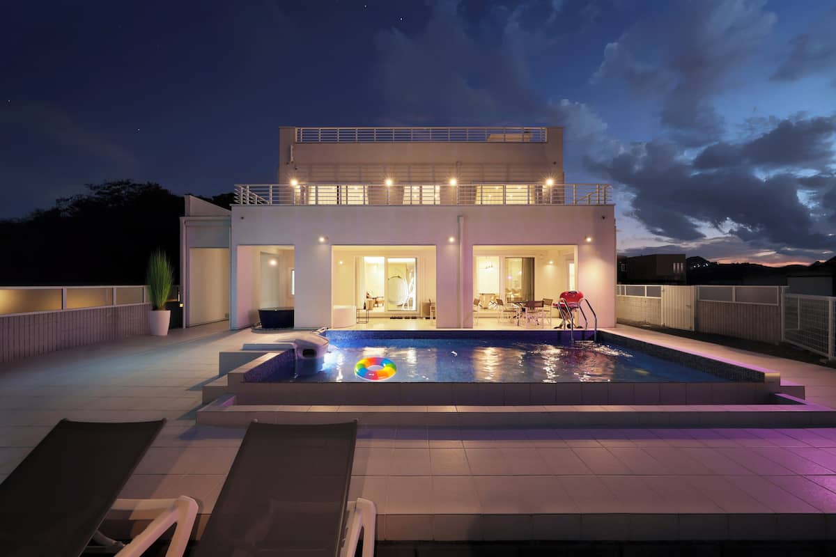 A modern two-story building with a swimming pool, outdoor seating, and a balcony.