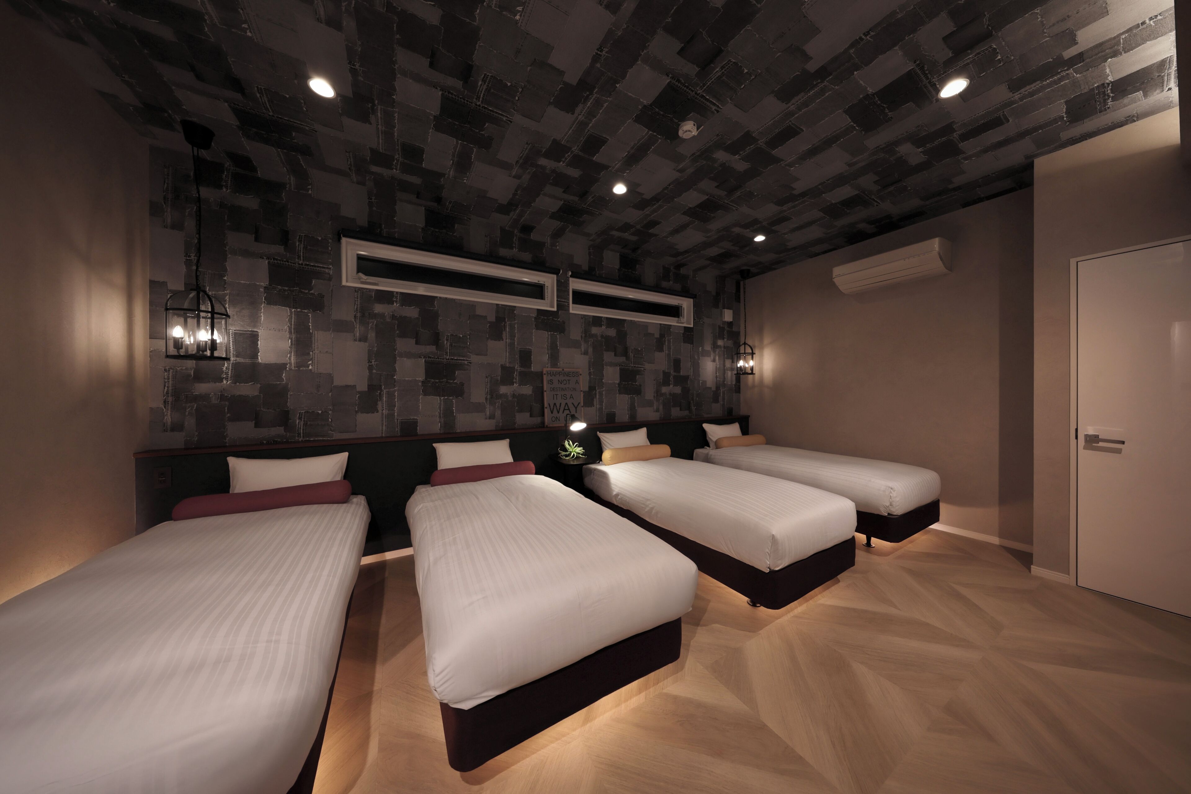 A modern hotel room with three beds, a brick-patterned ceiling, and a minimalist design.