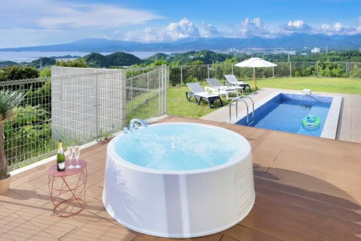 A hot tub on a patio with a view of mountains and a pool.