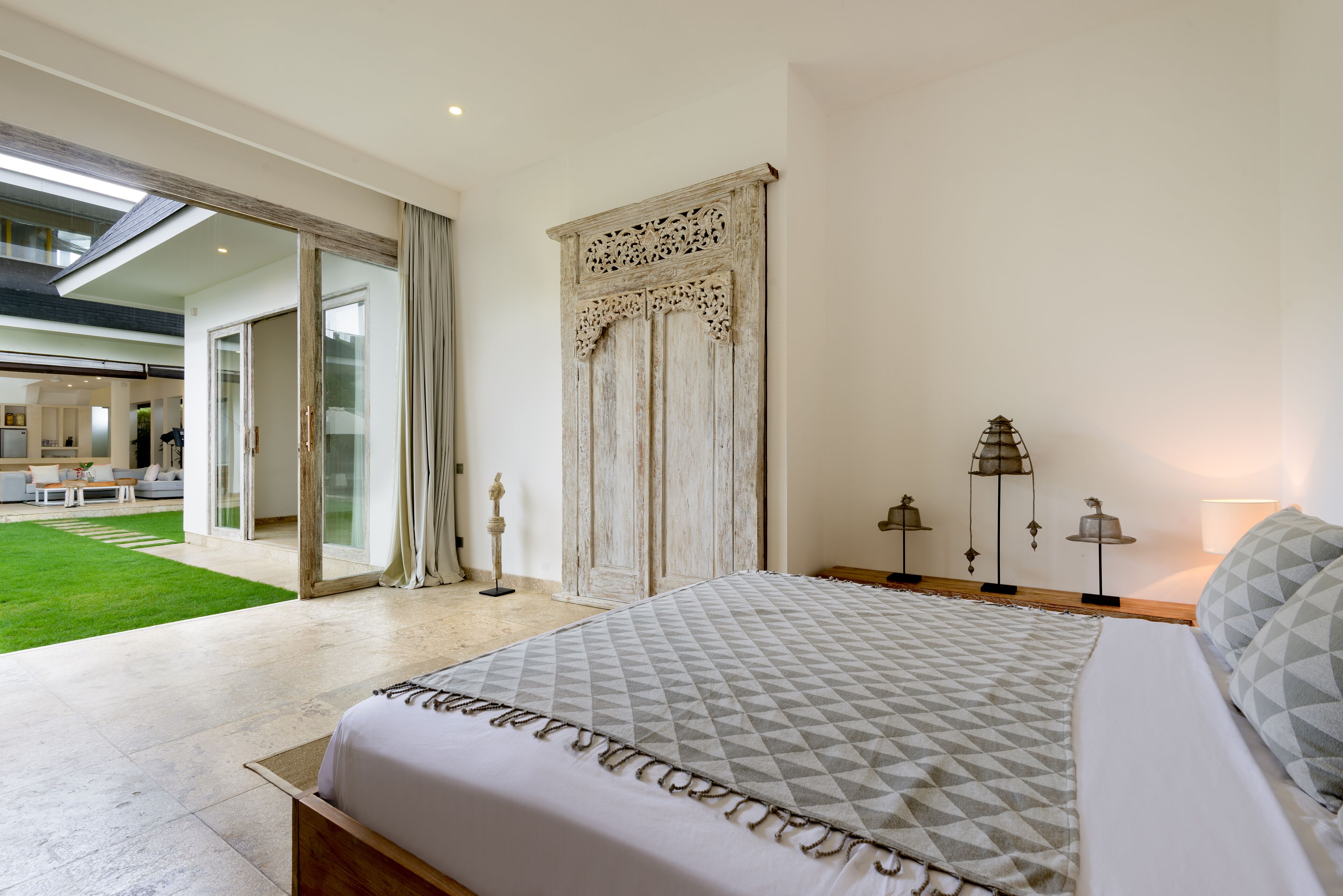 A spacious bedroom with a large bed, a sliding glass door leading to a balcony, and a decorative wall panel.