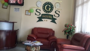 A hotel lobby with a brown leather sofa, a wooden reception desk, and a wall with a 'G' logo and 'HOTEL' text. - SGS Hotel (Addis Ababa)
